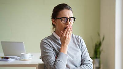 Девушка зевает и прикрывает рот рукой